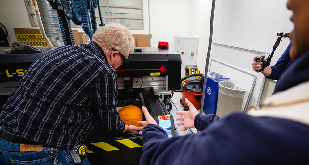 An engineering professor places a pumpkin in the laser cutter machine