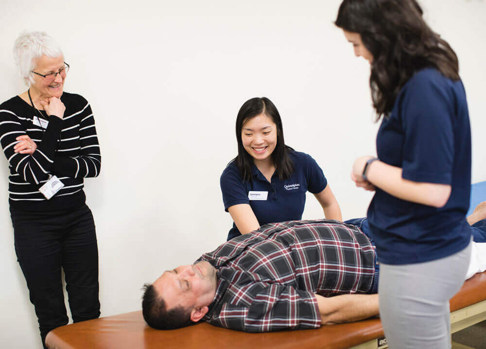 Professors aids two students help a patient laying on a table