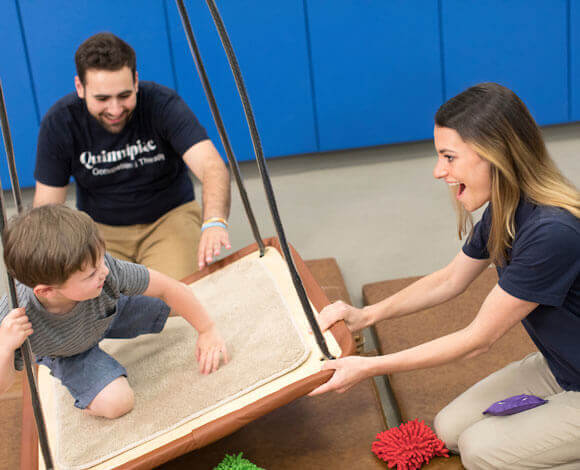 Two occupational therapy students work with a child on a swing board in the movement lab.