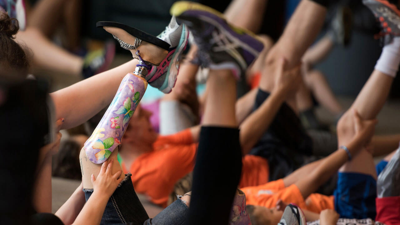 Students hold their legs and prosthetic limbs inn the air as part of a stretching exercise