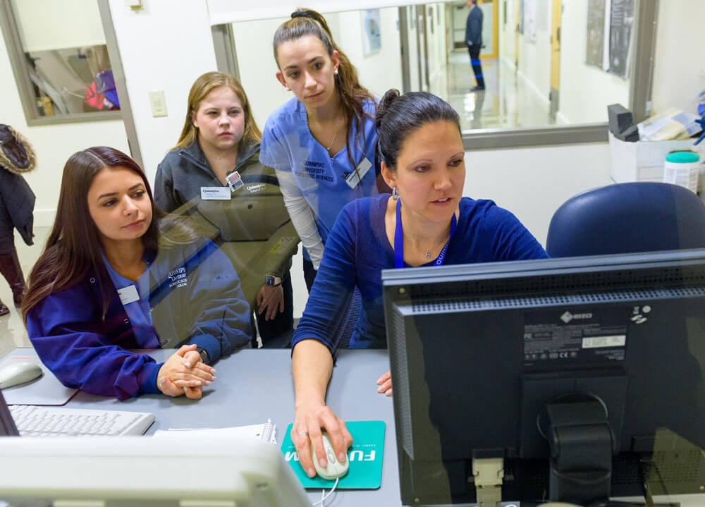 A professor and a group of students looking at a computer screen