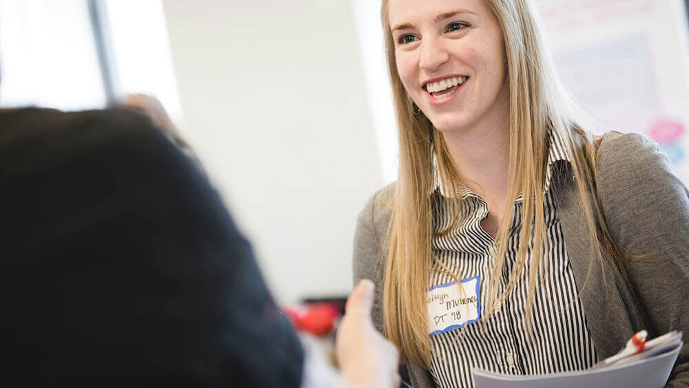 A student holds her notebook while talking to a job recruiter at a career fair