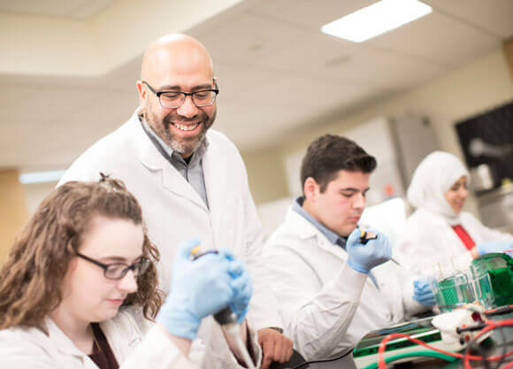 A professor guides students through a laboratory procedure.