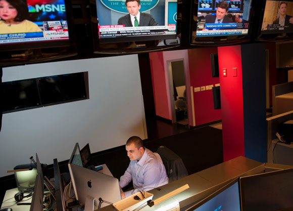 An alum works at his desk at Fox News surrounded by tv screens