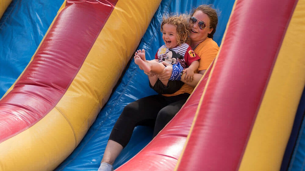 A health sciences student holds a child as they go down a slide