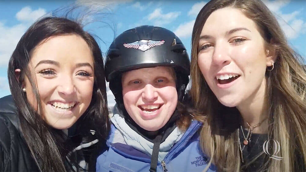 Two health sciences students smile with a skiing camp participant, starts video