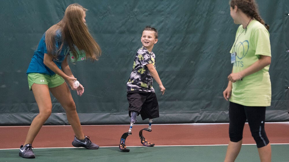 Two health sciences students play a game with a child wearing leg blades