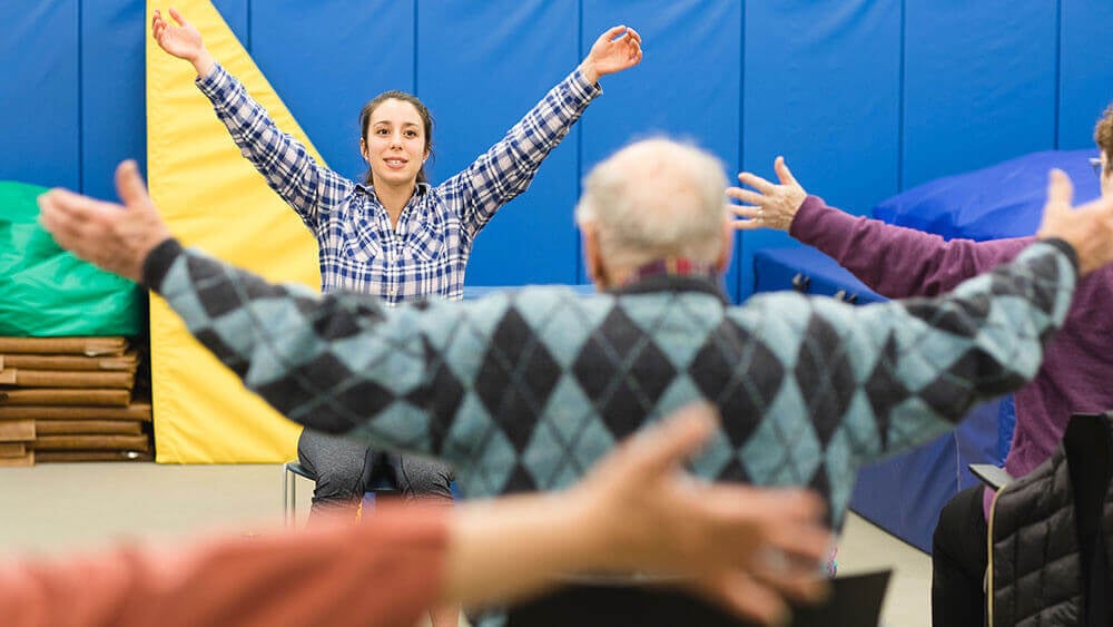 A health sciences student reaches her hands to the sky in leading a class for seniors