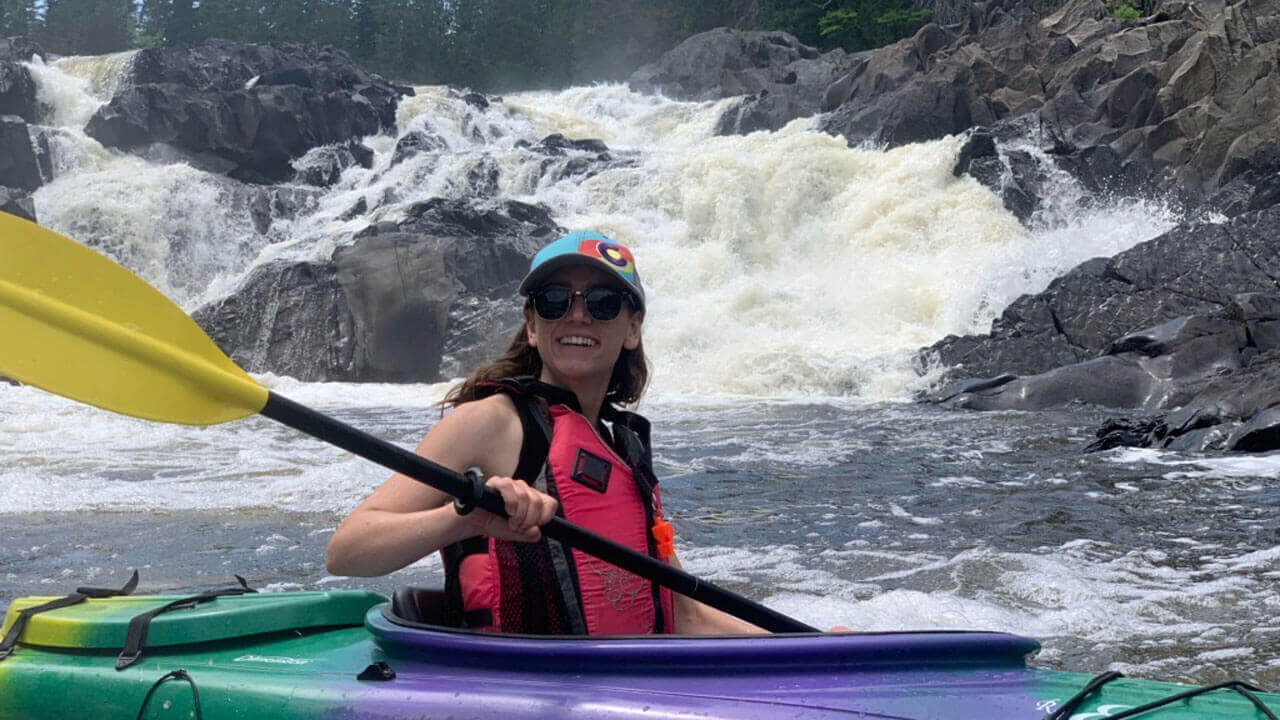 A woman in a colorful kayak with rapids rushing behind her.