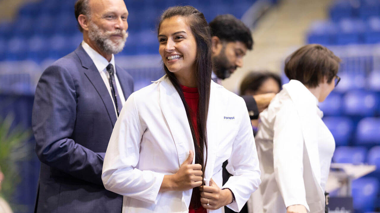 A student smiles as she receives her medical white coat