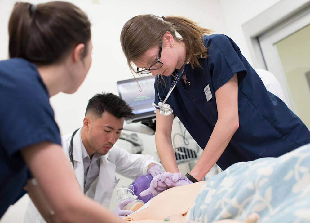 Three nursing students administer treatment and perform CPR on a simulation dummy