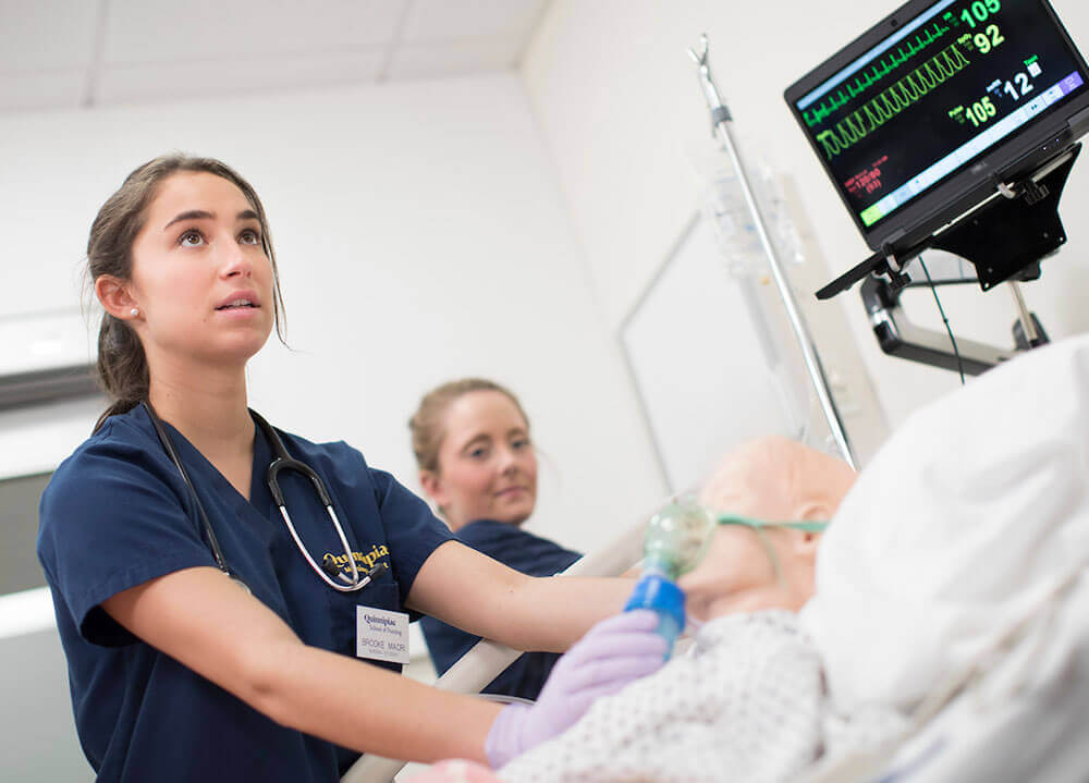 A nursing student examines a patient mannequin in the School of Nursing simulation suite
