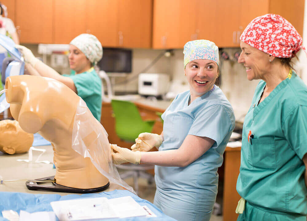 A nursing student wearing scrubs practices administering an epidural on a medical dummy