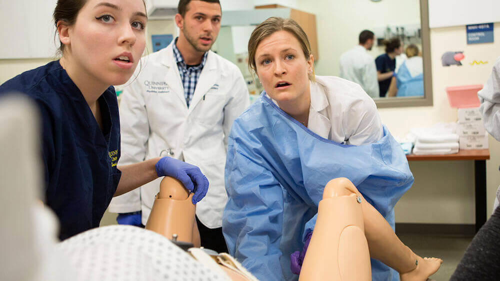 Three Quinnipiac students in scrubs deliver a baby during a simulated birth exercise