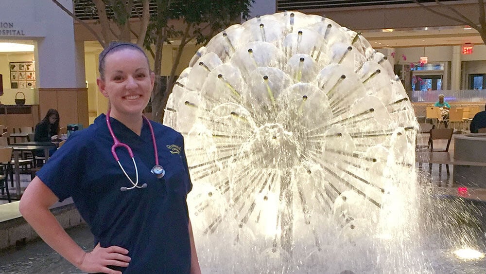 A nursing student poses in scrubs outside of a medical center