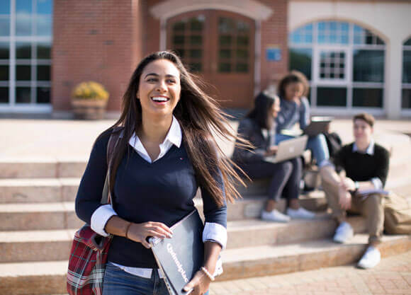 A student holding a Quinnipiac folder walks by the library steps