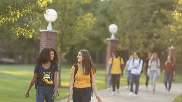 A dozen students in Quinnipiac shirts walk across campus