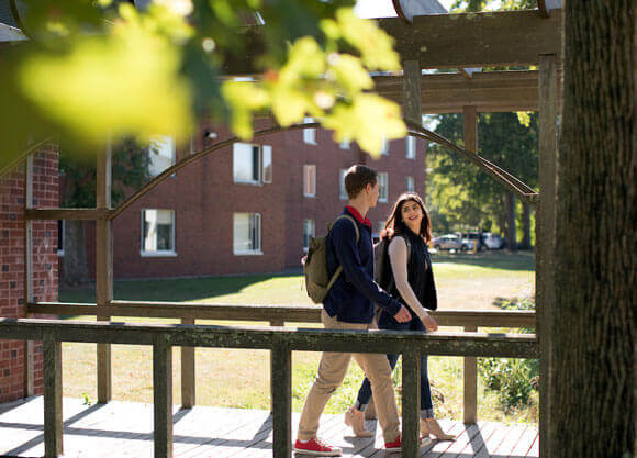 Two students walk over a wooden bridge on campus.