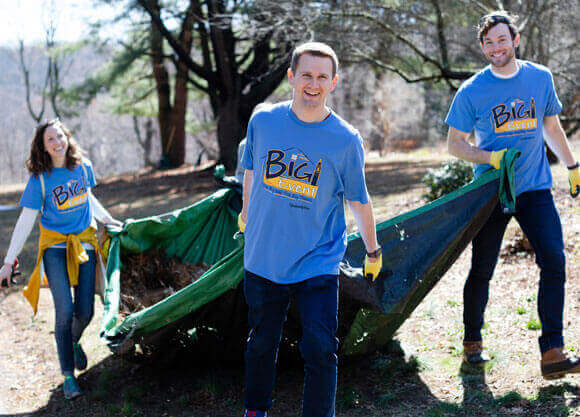 Three students wearing "Big Event" shirts move a pile of leaves at Edgerton Park.