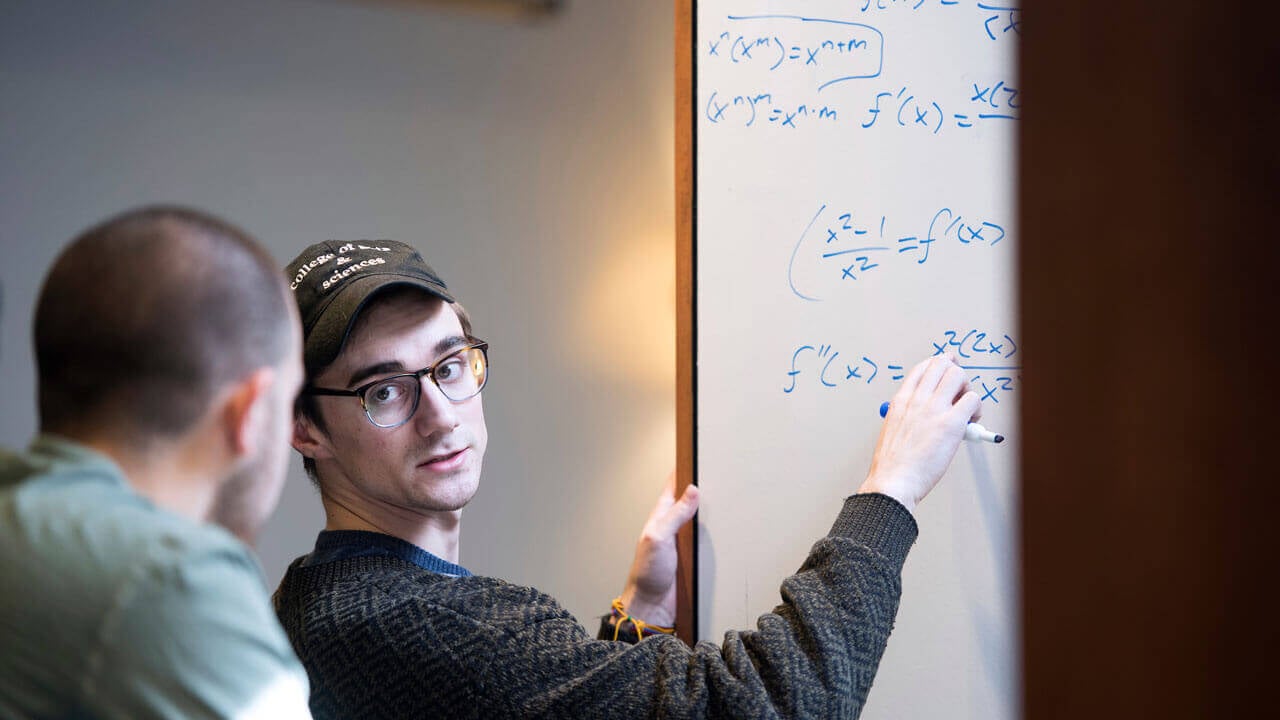 Jason Culmone tutors a student while writing on the white board.