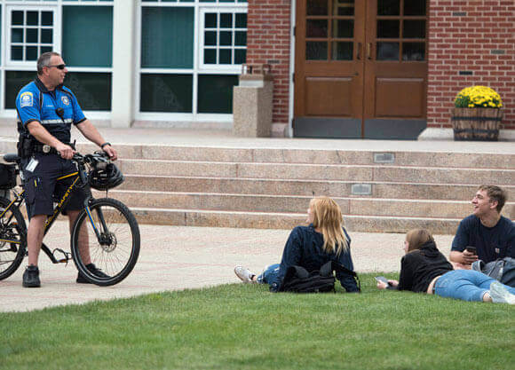 A Public Safety officer on a bike speaks with students laying on the grass.