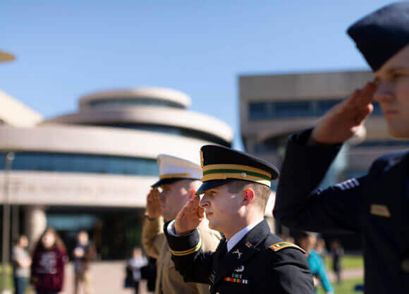Three student veterans salute during a ceremony