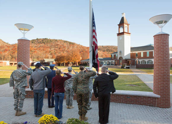 Student veterans salute in front of the American flag during a ceremony