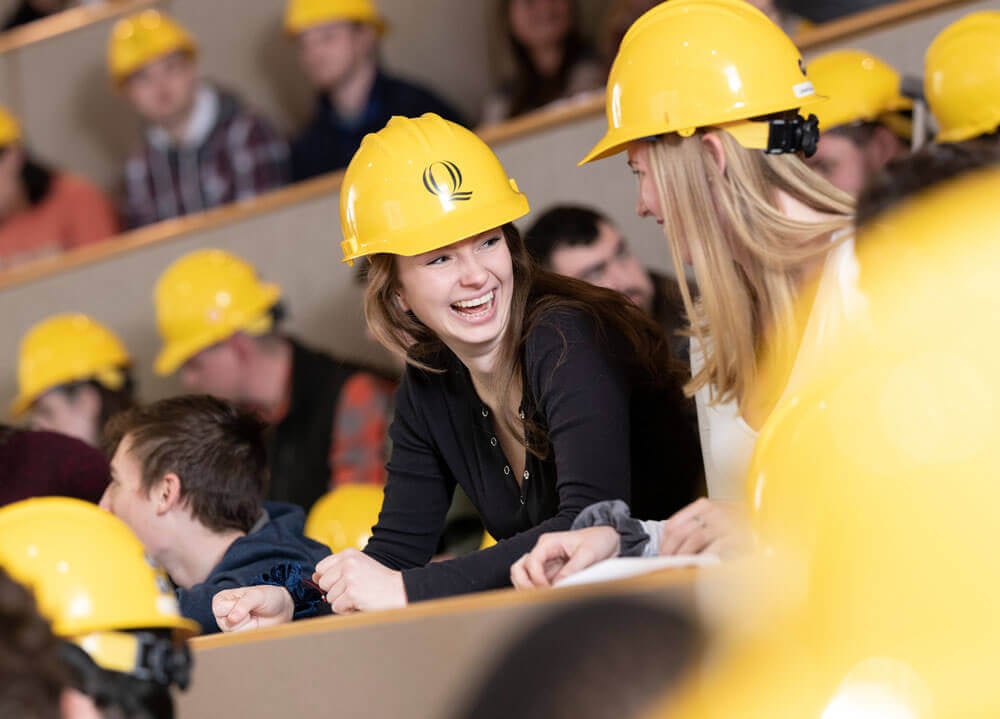 A female student smiles with a gold hard hat on her head.