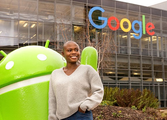 Brittany Hayles stands next to an Android statue outside of a building with a Google sign on it.