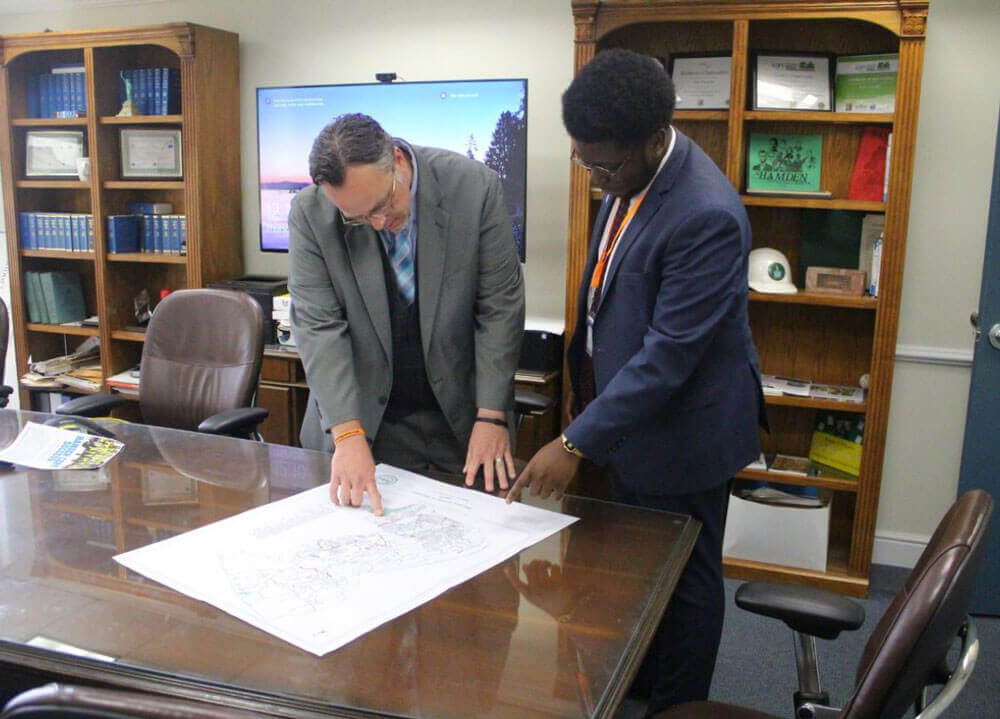 A male student with the mayor of Hamden looking and pointing at a map on a conference table.