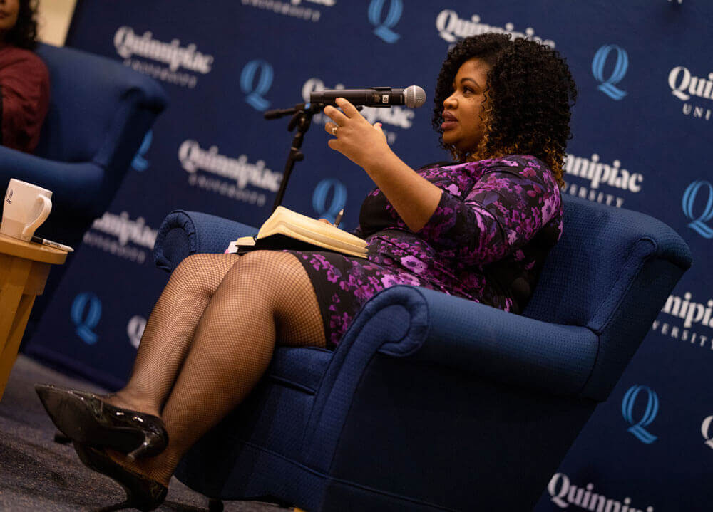 Khalilah Brown-Dean sits in a comfy chair with her book, speaking into a microphone.