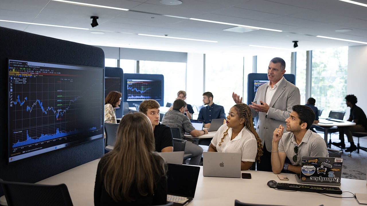 Individuals sit around table while looking at a graph on a screen