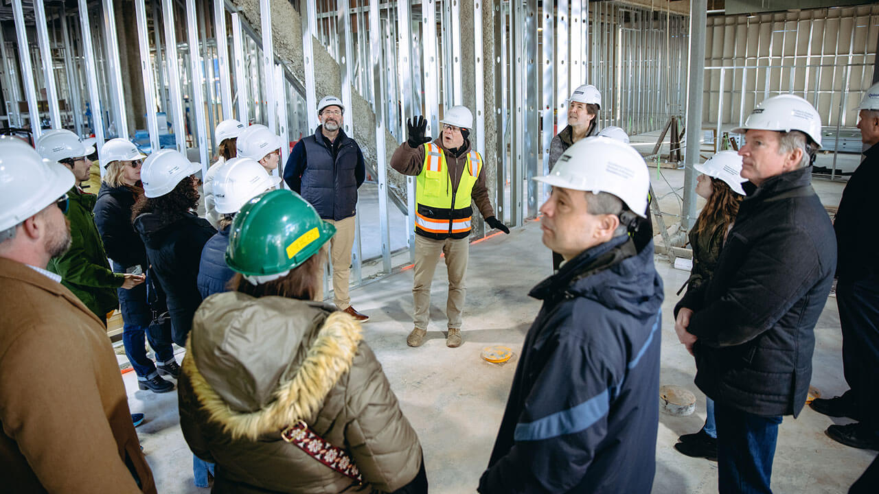A group of QU staff on a construction site listening to a construction worker speak.