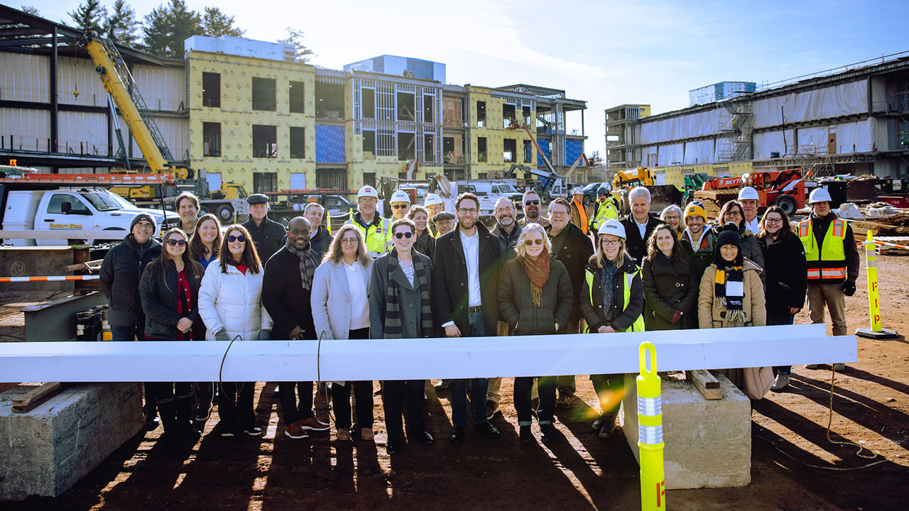 Quinnipiac staff pose for a group photo with a beam that will be placed on a building on the South Quad.
