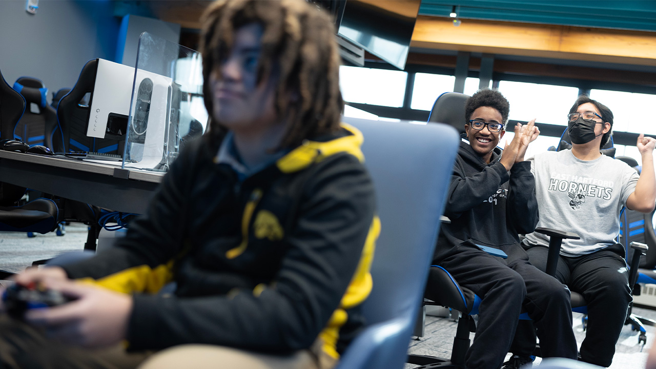 Two students in the background cheer on an eSports athlete competing in the foreground.