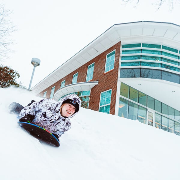 A student laughs as she sleds down a hill behind the Quinnipiac library