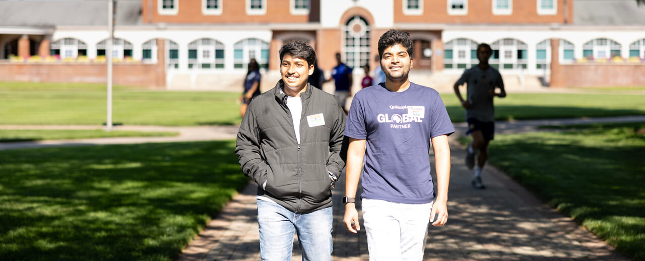A global partner volunteer walks with an international student across the quad