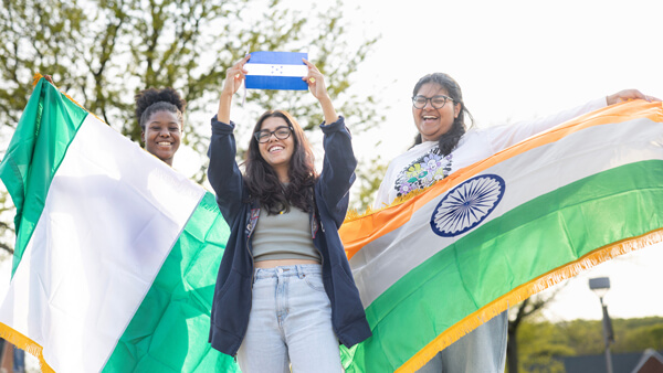 3 international students hold up their country's flag on the Quinnipiac quad