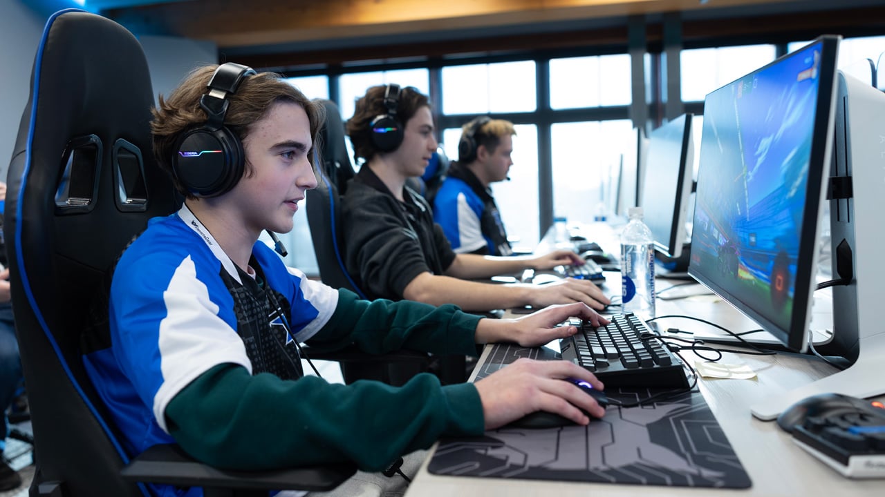 A student sits at a gaming computer wearing headphones.