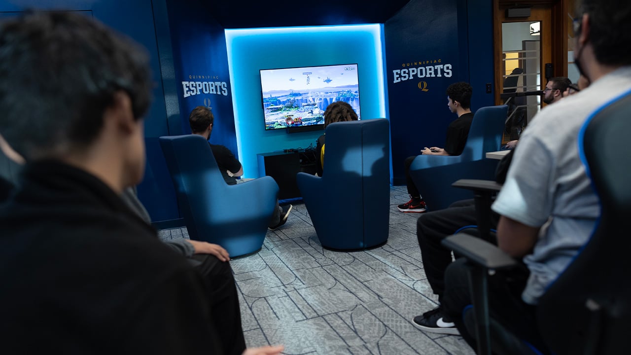 Students all crowd around a screen in the Quinnipiac eSports room.