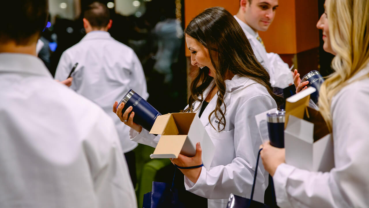 Student opens a personalized cup as a gift after their white coat ceremony.